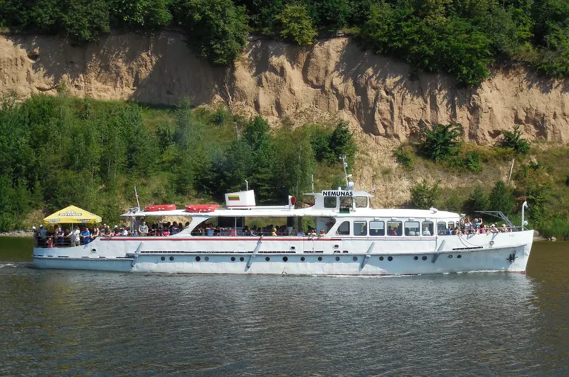 Laivas „Nemunas“ plaukia prie stataus miškingo kranto