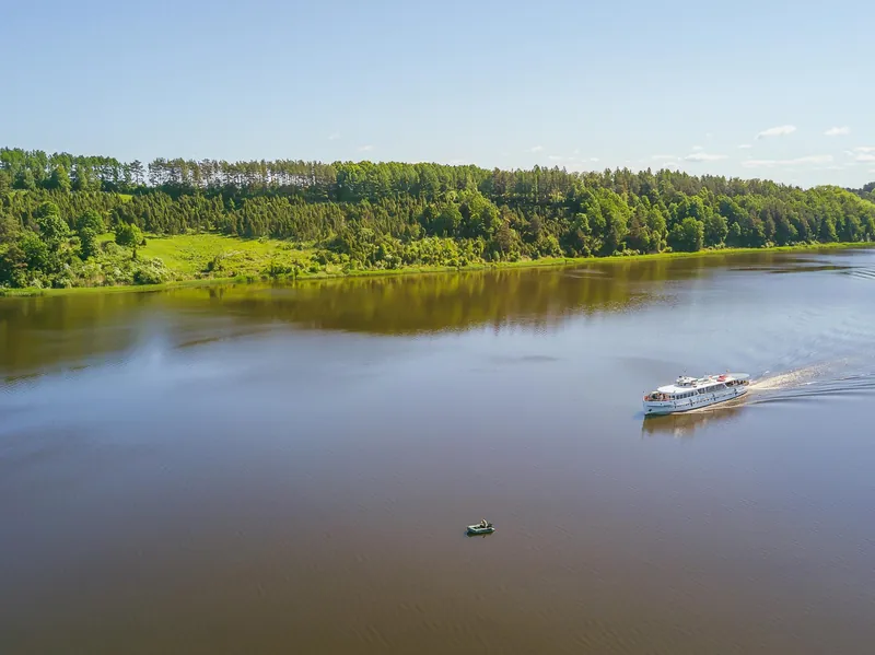 Laivas plaukia tarp miškingų krantų